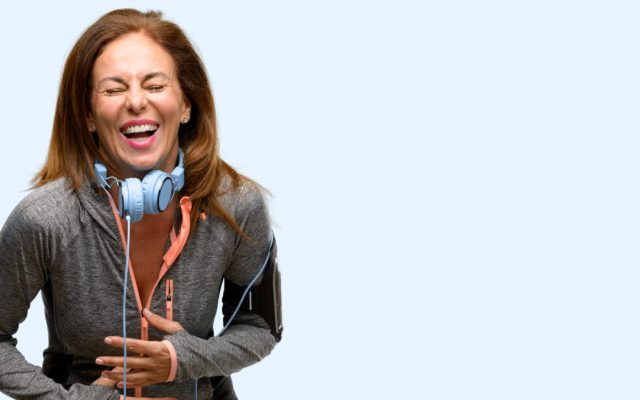 Middle age gym fit woman with workout headphones confident and happy with a big natural smile laughing isolated blue background